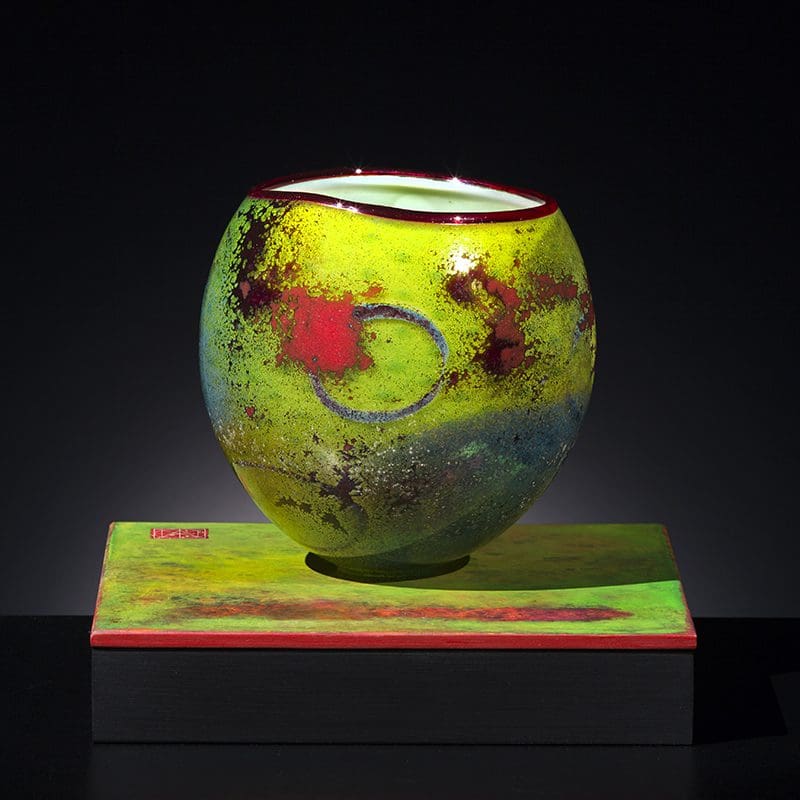 A yellow vase with red and green swirls on top of it.