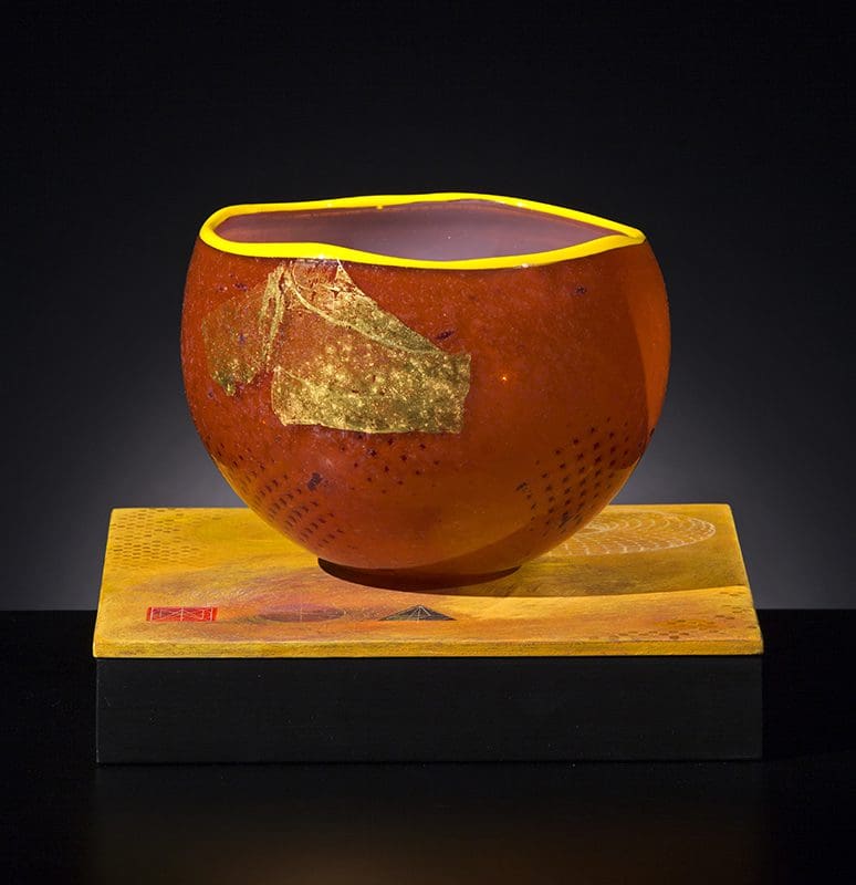 A red bowl with yellow rim on top of a wooden block.
