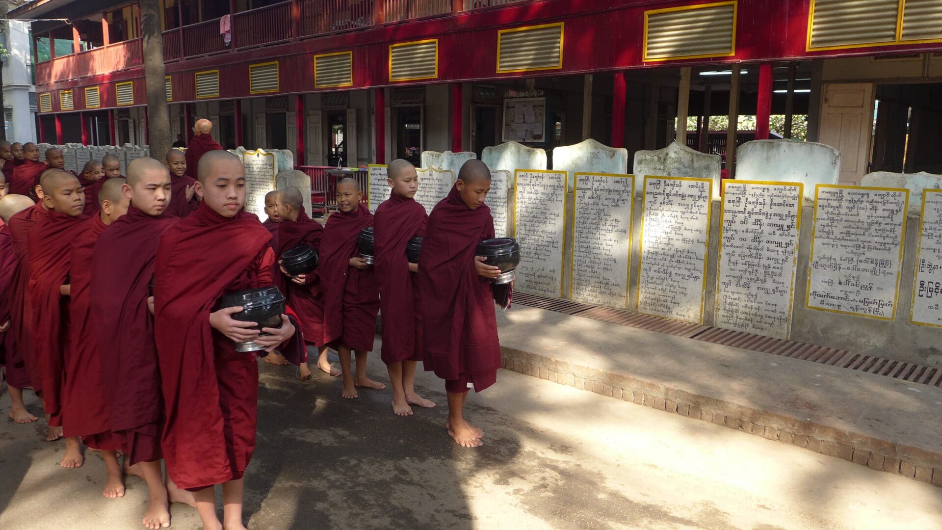A group of young monks in red robes holding black objects.
