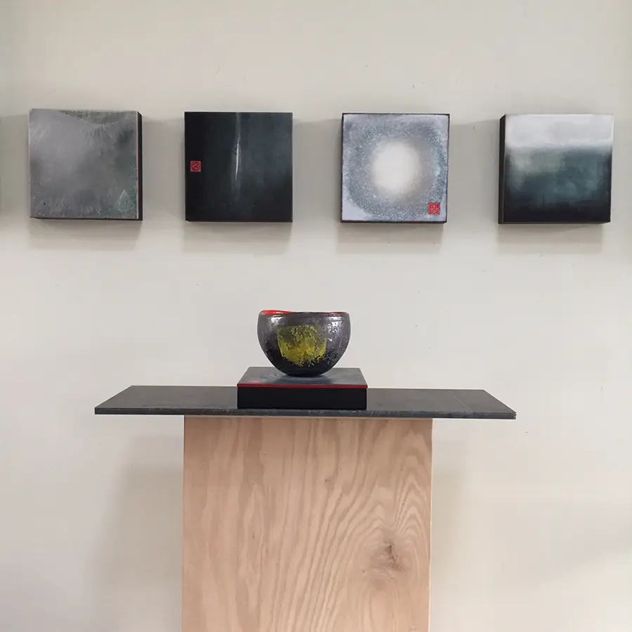 A bowl on top of a table in front of four paintings.