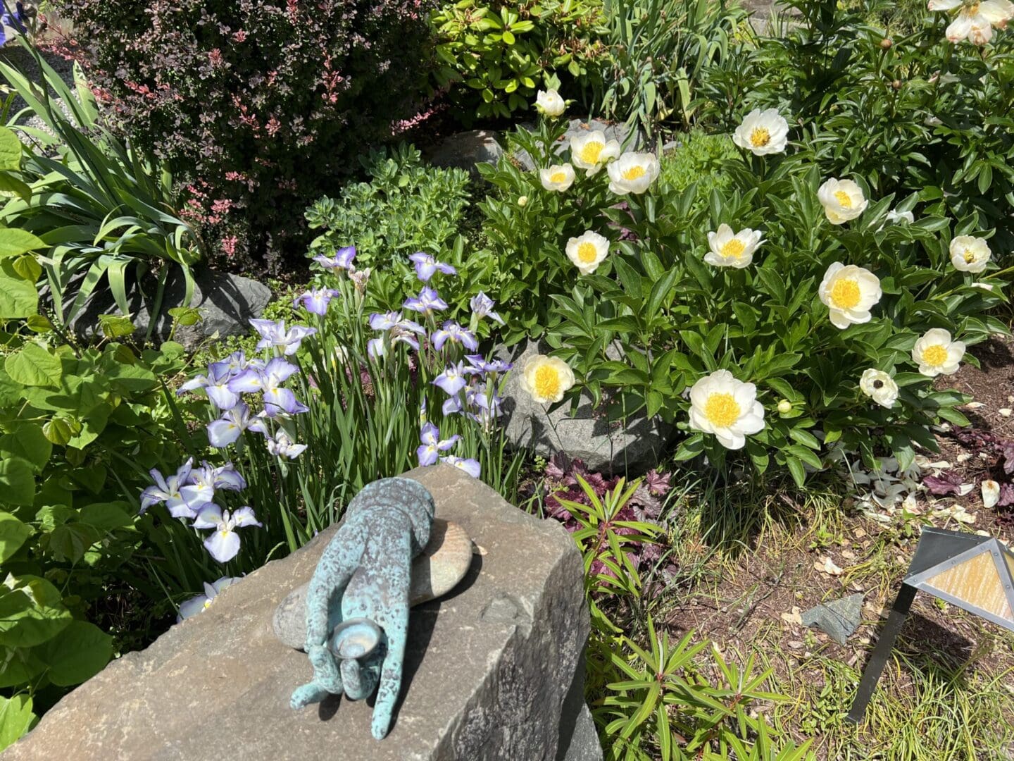 A statue of a frog on top of a rock in front of flowers.