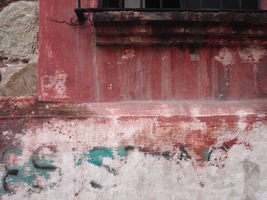 A red wall with peeling paint and a window.
