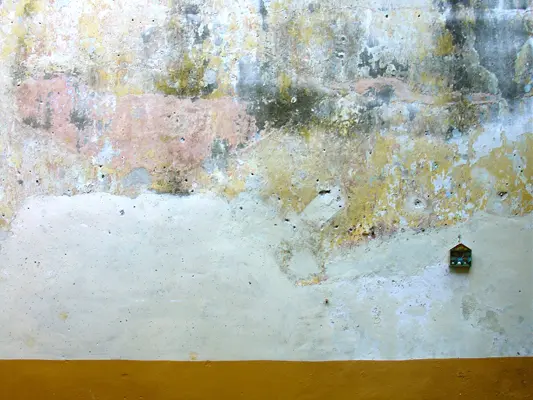 A wall with peeling paint and yellow trim.